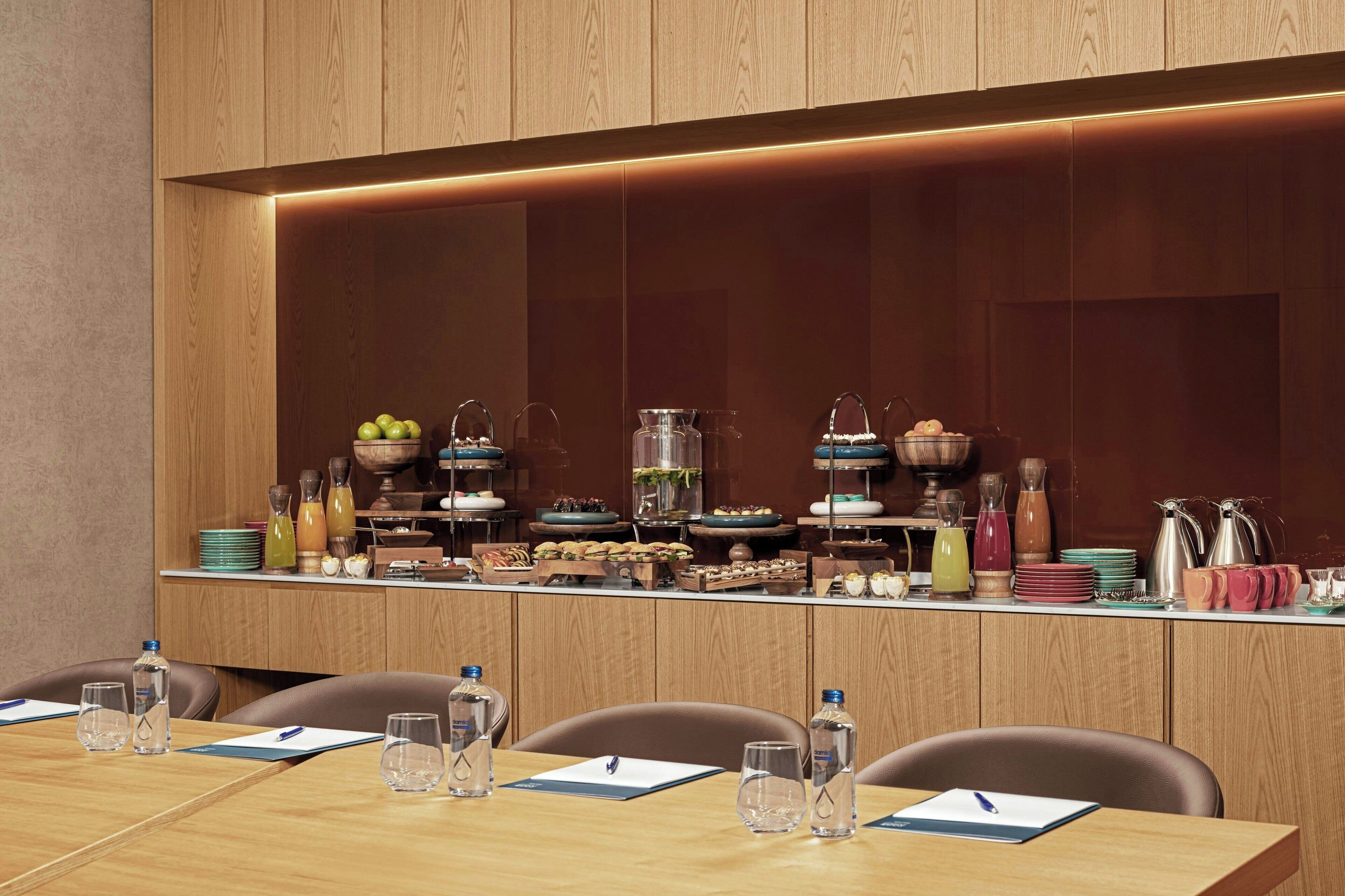 A conference room with a long table, chairs, and a buffet setup with various food items and beverages.