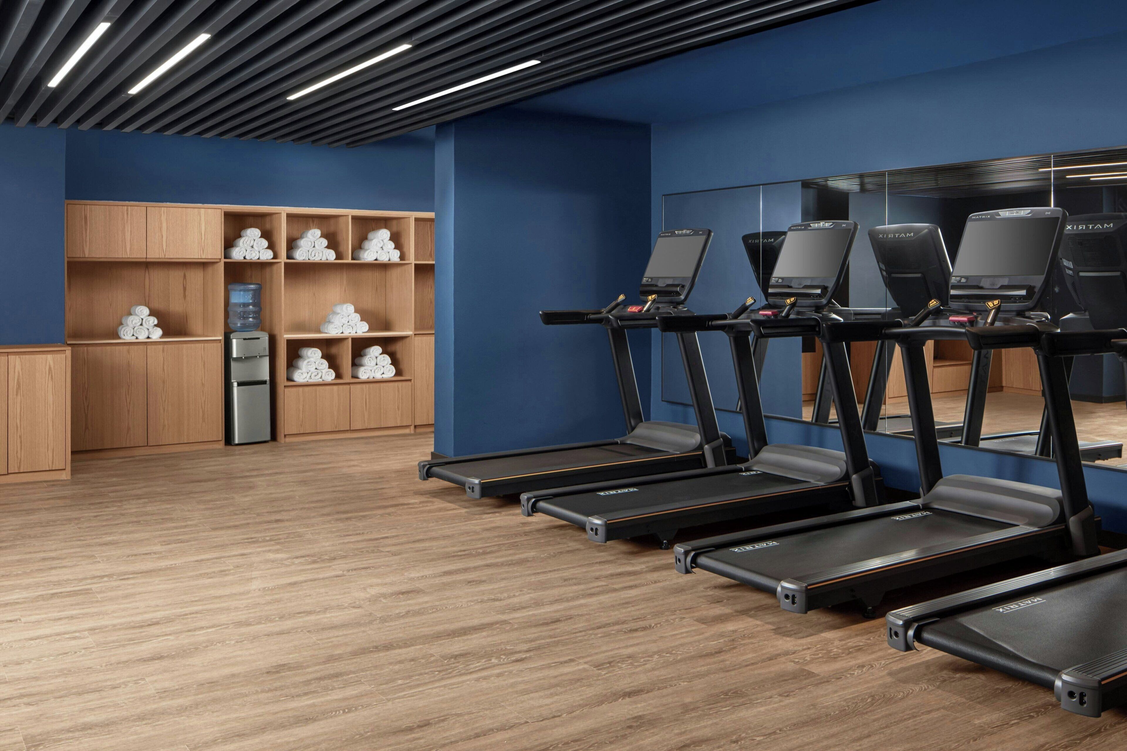 A fitness room with treadmills, wooden cabinets, and a water dispenser.