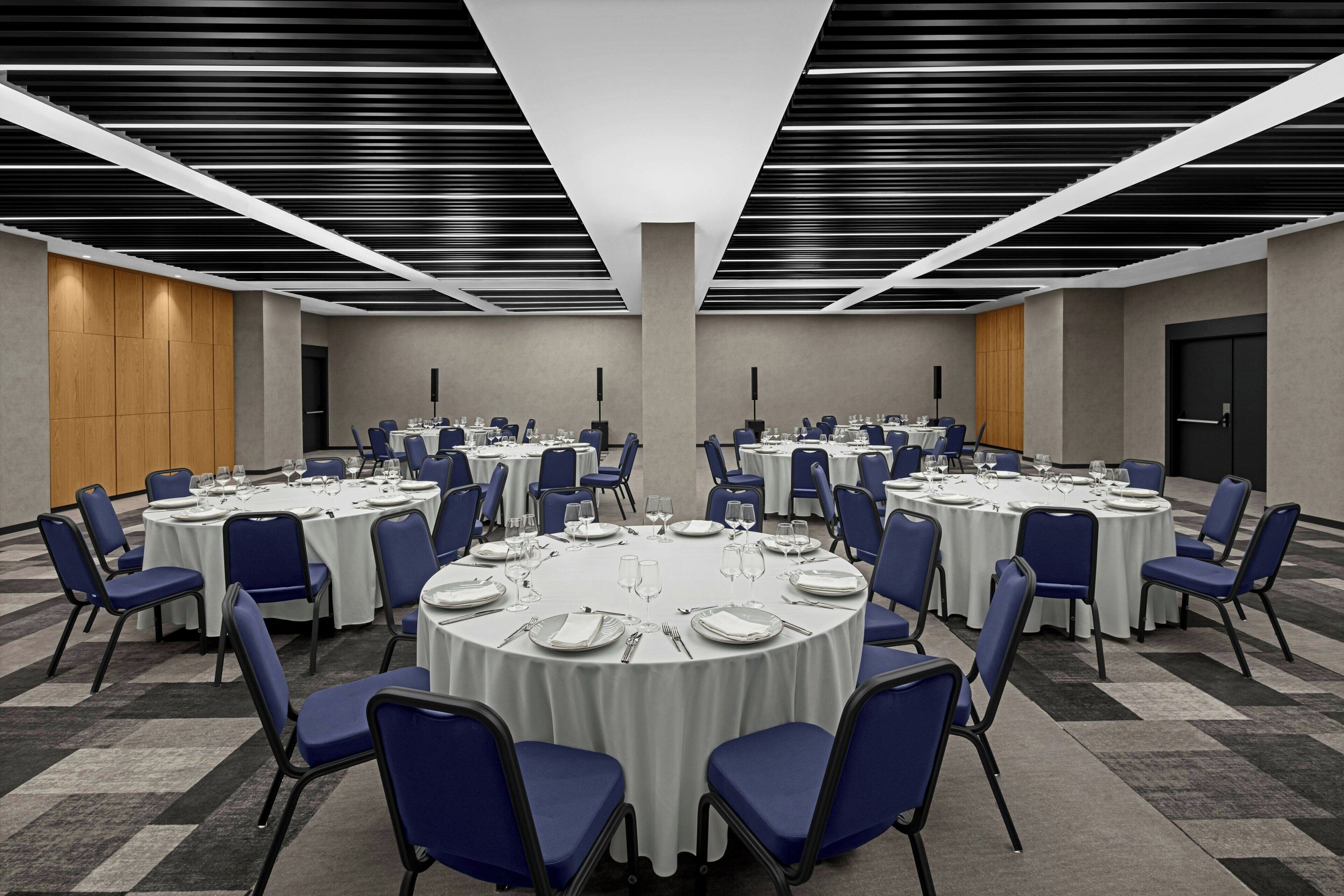 A conference room with round tables, blue chairs, and white tablecloths.