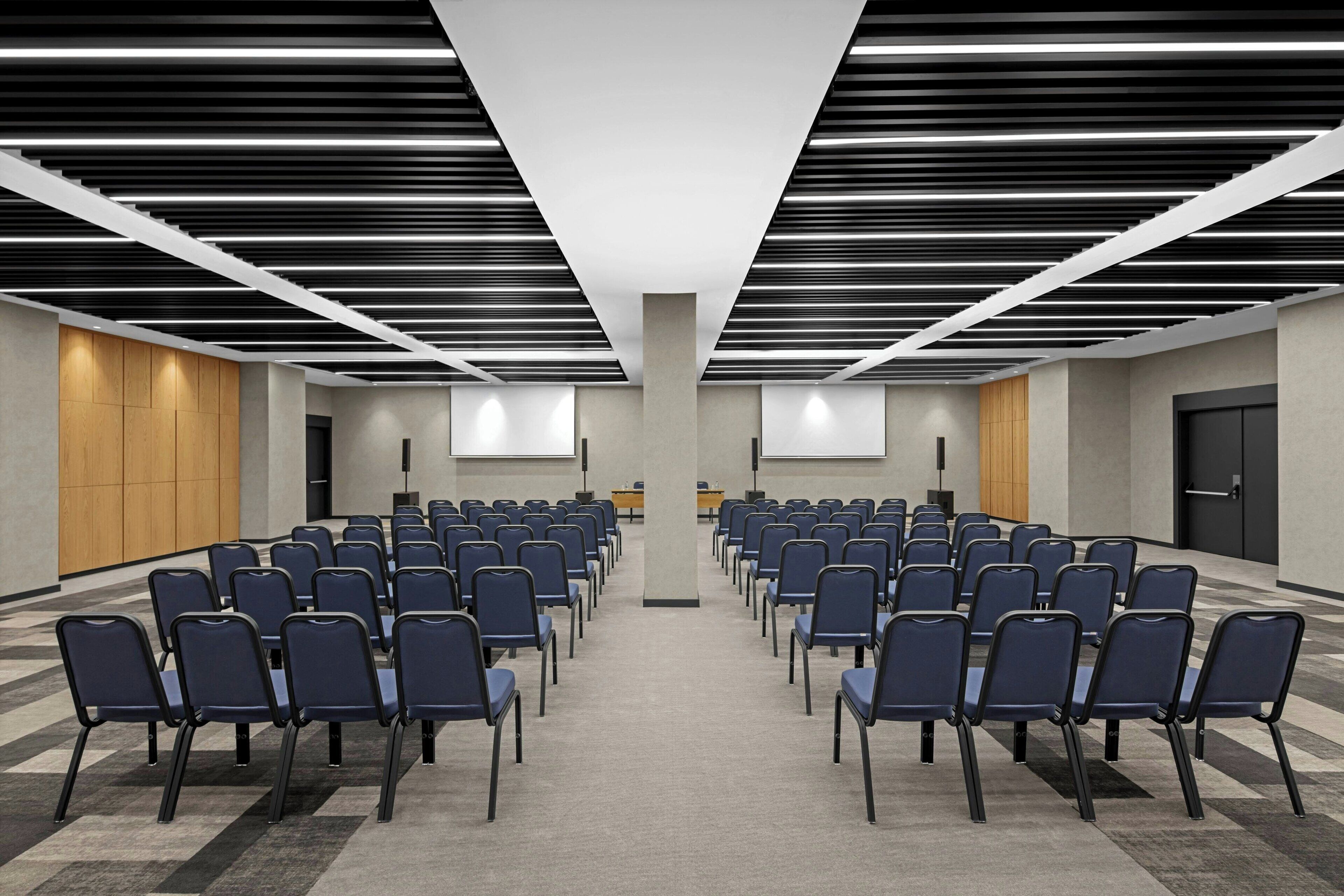 Une salle de conférence avec des rangées de chaises, un écran de projection et un pupitre.