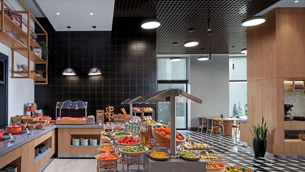Un buffet proposant une variété de plats, ainsi qu’un espace cuisine moderne doté de meubles en bois et d’un sol carrelé.