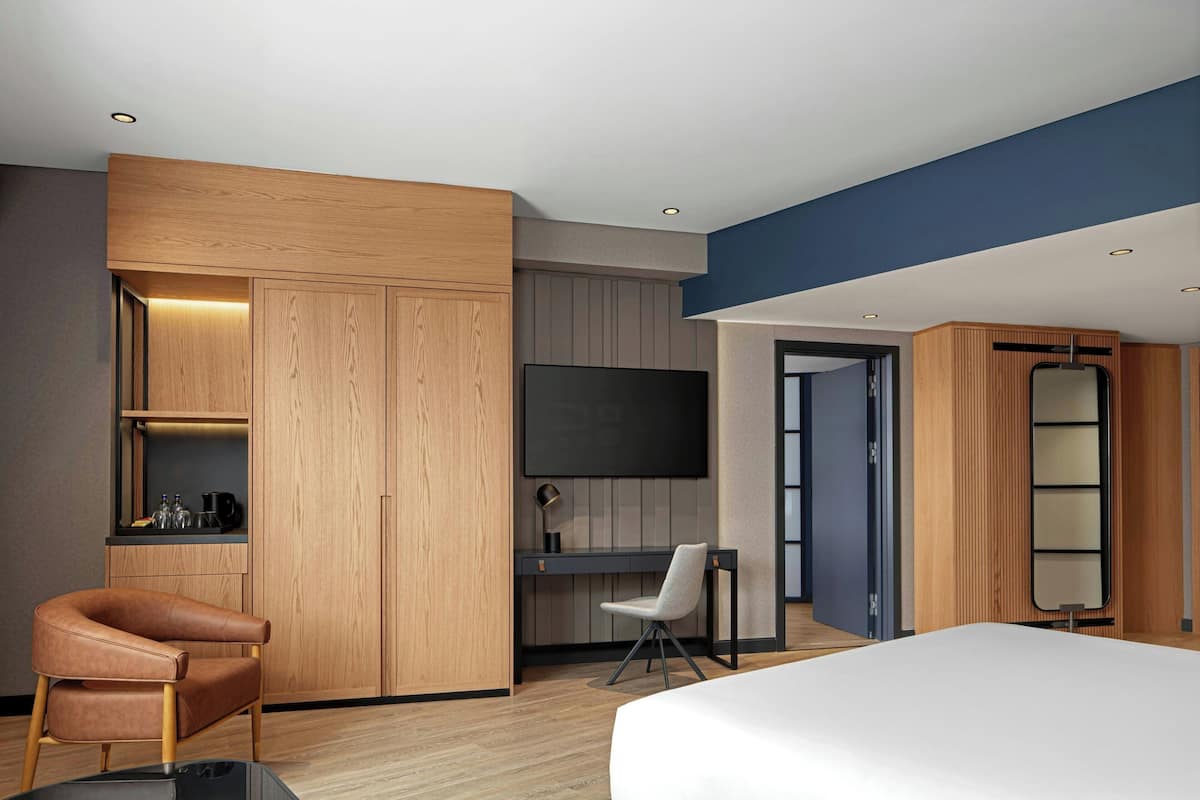 Une chambre d’hôtel moderne équipée d’une armoire en bois, d’un bureau avec une chaise, d’un téléviseur à écran plat et d’un lit.