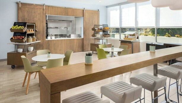 A modern kitchen with wooden cabinets, a large island, and a view of the outdoors. - Element by Marriott Savannah Midtown (Savannah)
