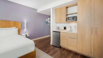 Ein modernes Hotelzimmer mit einem hölzernen Bett, einer kleinen Küchenzeile und einem kompakten Badezimmer.