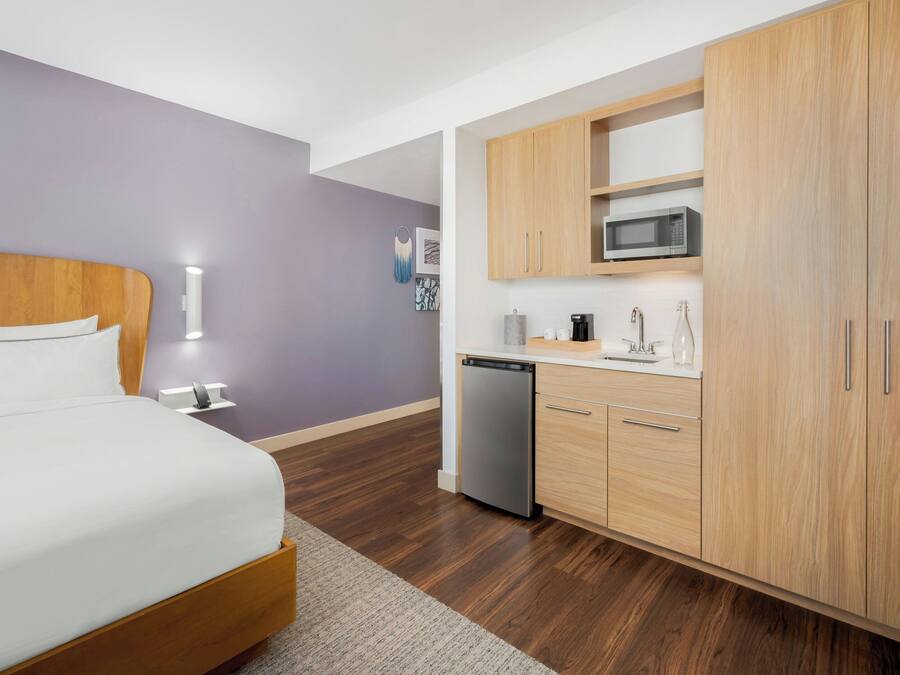 Ein modernes Hotelzimmer mit einem hölzernen Bett, einer kleinen Küchenzeile und einem kompakten Badezimmer.