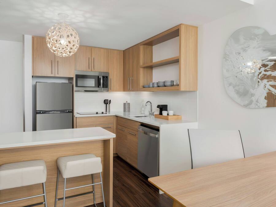 A modern kitchen with wooden cabinets, stainless steel appliances, a white countertop, and a bar area with stools.
