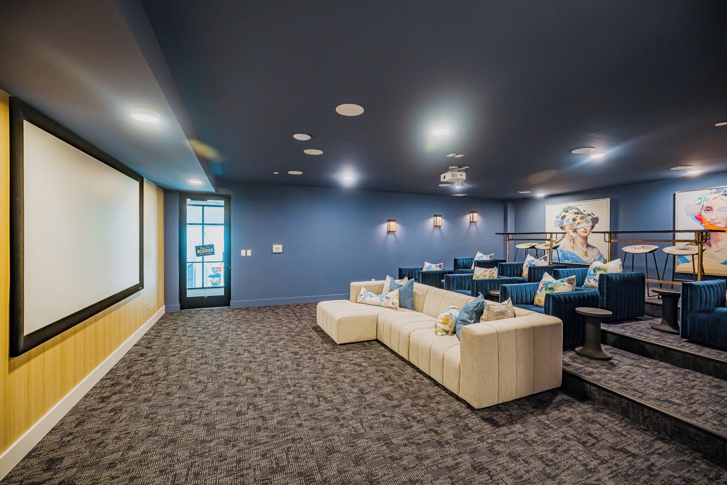 A movie theater with a large screen, multiple rows of seating, and a carpeted floor.