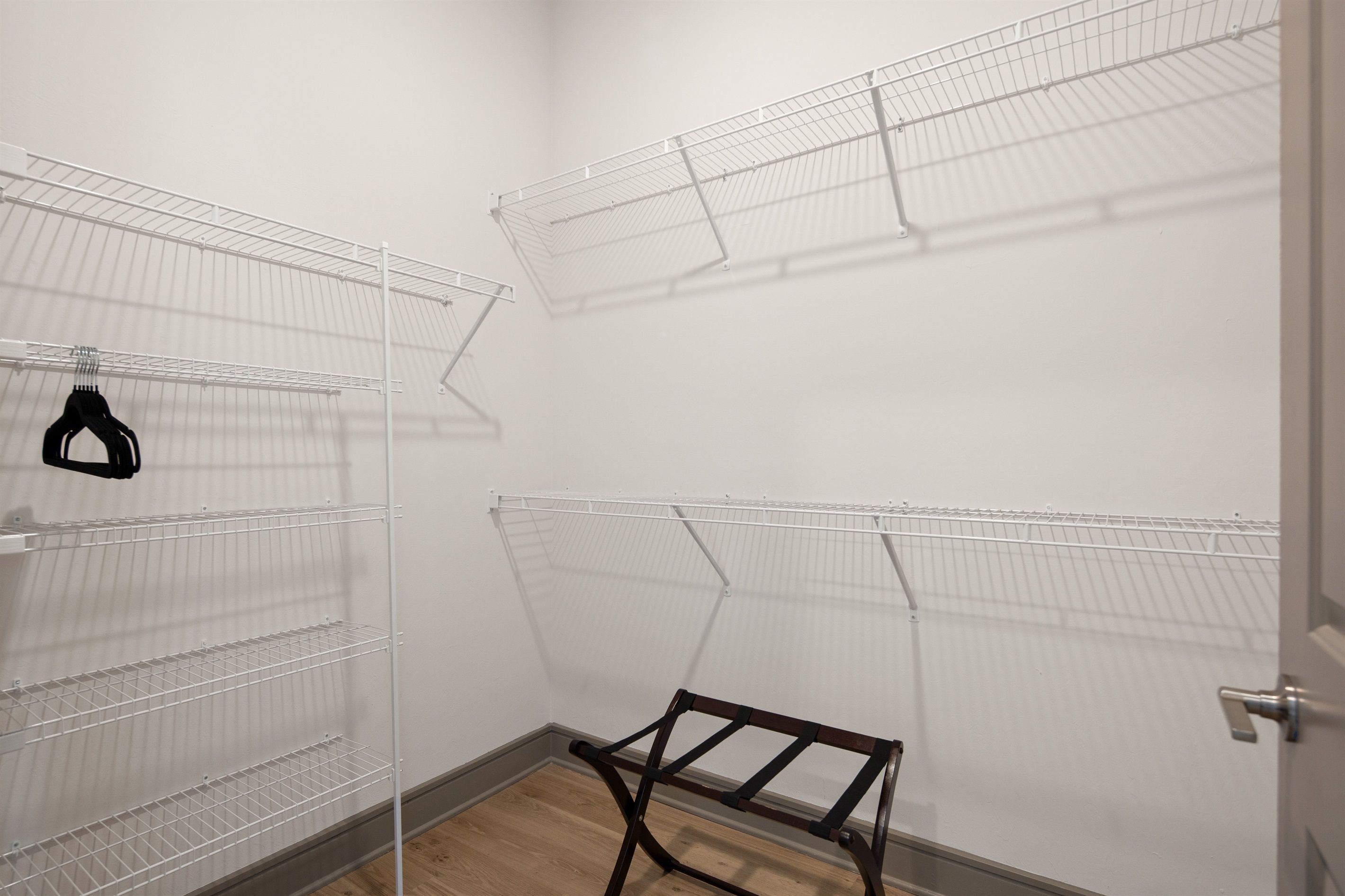 A walk-in closet with multiple wire shelving units and a wooden rack.