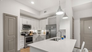 A modern kitchen with white cabinetry, stainless steel appliances, and a large island with a sink. - Beachy Escape: Communal Pool, Gym, and Theater (Naples)