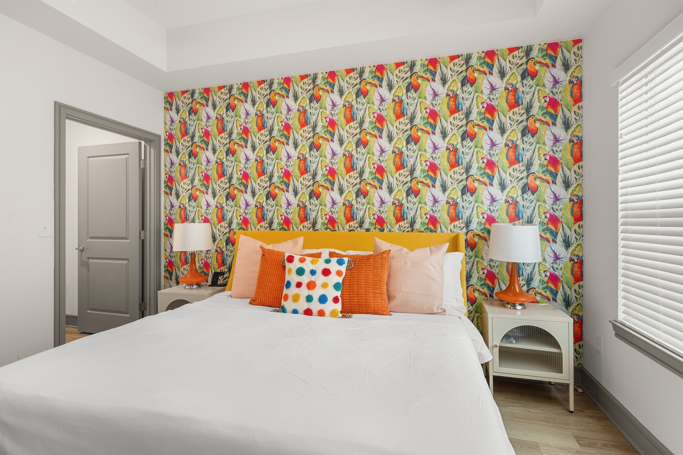 A bedroom with a bed, two bedside tables, and a colorful tropical wallpaper.
