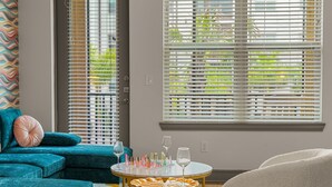 Ein Zimmer mit türkis-weißen Möbeln, einem runden Tisch mit Weingläsern und einem Fenster mit Jalousien.