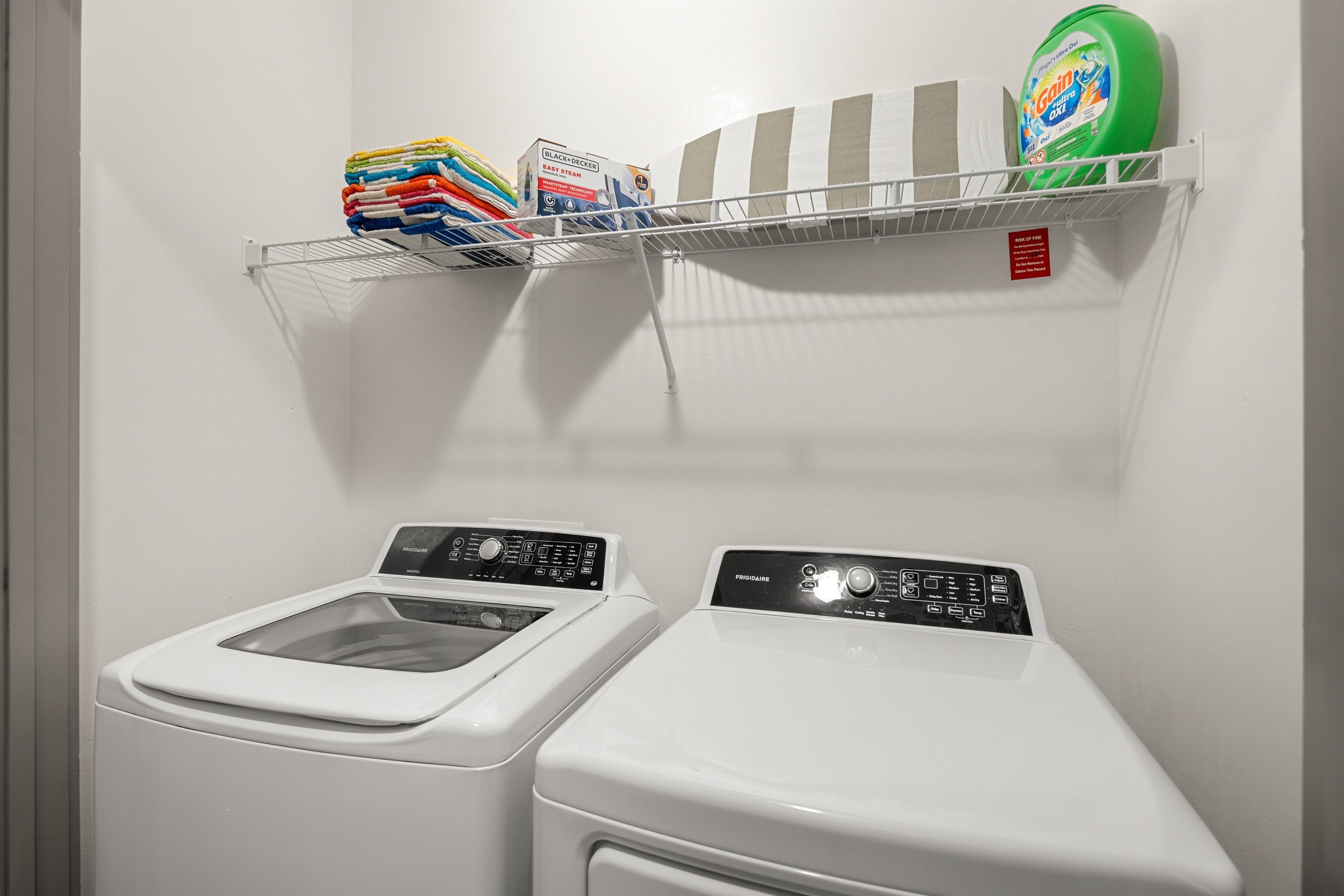 A laundry area with two washing machines, a shelf with folded clothes, and a detergent box.