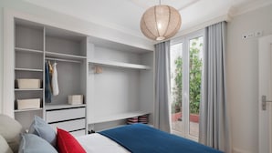 Ein Schlafzimmer mit Bett, Kleiderschrank, Pendelleuchte und Blick durch ein Fenster.