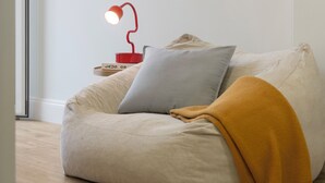 Ein gemütliches Zimmer mit Sitzsack, einem kleinen Beistelltisch mit roter Lampe und einem gerahmten Kunstwerk an der Wand.