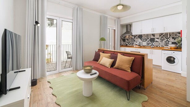 Un salon moderne avec un canapé rouge, une table basse blanche et un tapis vert. On y trouve également un coin cuisine avec des meubles blancs et un lave-linge.