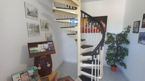 Una escalera de caracol con barandilla blanca y escalones negros, rodeada de cuadros enmarcados en las paredes.
