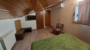 Un dormitorio con techo de madera, colcha verde, una silla y un ventanal pequeño.