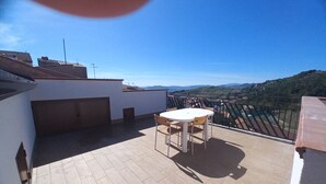 Una terraza en la azotea con mesa y sillas, que ofrece vistas a un paisaje montañoso.