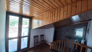 Una habitación con techo de madera, dos ventanas, una escalera y un pequeño rincón de cocina.