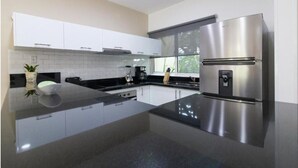 Une cuisine moderne avec des meubles blancs, un réfrigérateur en acier inoxydable et un plan de travail noir.