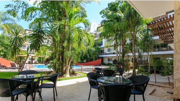 Un espace extérieur aménagé en terrasse, avec des tables et des chaises rondes, entouré de palmiers et d’une piscine.