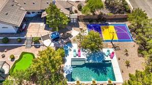 An aerial view of a residential property with a swimming pool, a basketball court, and a patio area.