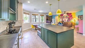 A modern kitchen with a central island, pendant lighting, and a vibrant mural on the wall.