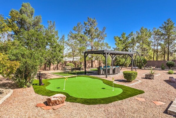 A golf putting green with a gazebo, seating area, and surrounding trees.
