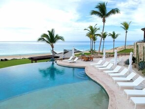 A pool area with lounge chairs and palm trees, overlooking a beach and ocean.