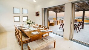 Een eetruimte met een houten tafel voor zes personen, een plafondventilator en uitzicht op de omgeving door grote schuifdeuren.
