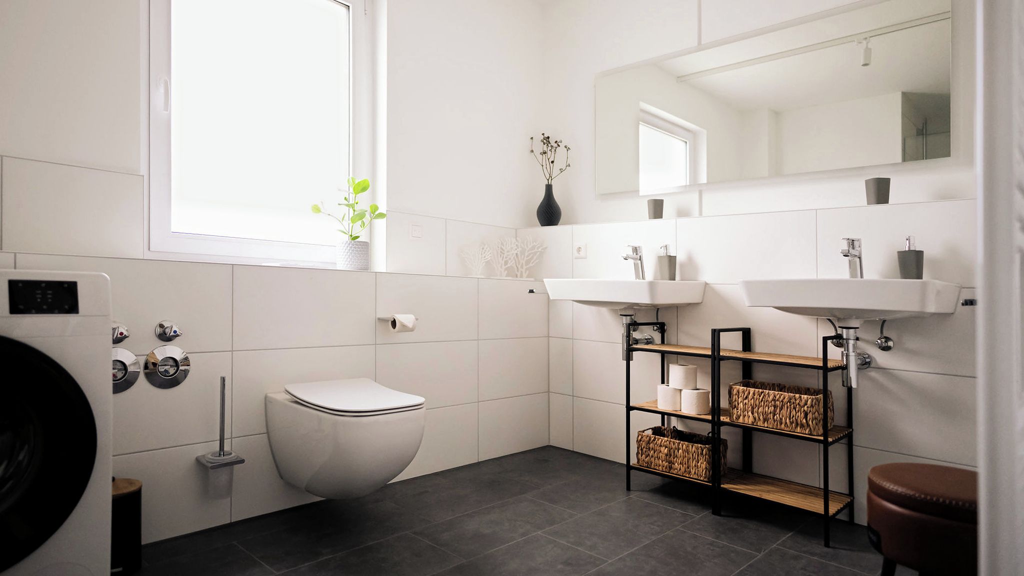 A modern bathroom with a toilet, a sink, a mirror, and a window.