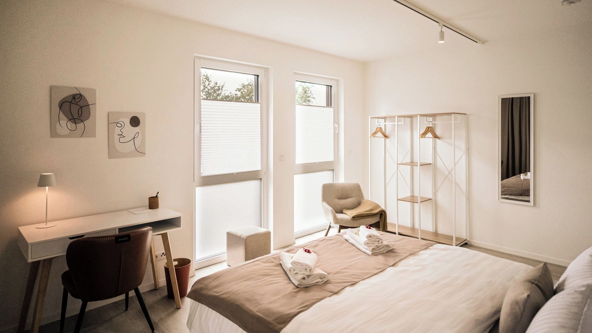 Ein modernes Hotelzimmer mit Bett, Schreibtisch, Stuhl und einem Kleiderschrank mit Ablagefläche.