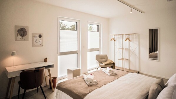 Una habitación de hotel moderna con cama, escritorio, silla y armario con espacio para colgar ropa.