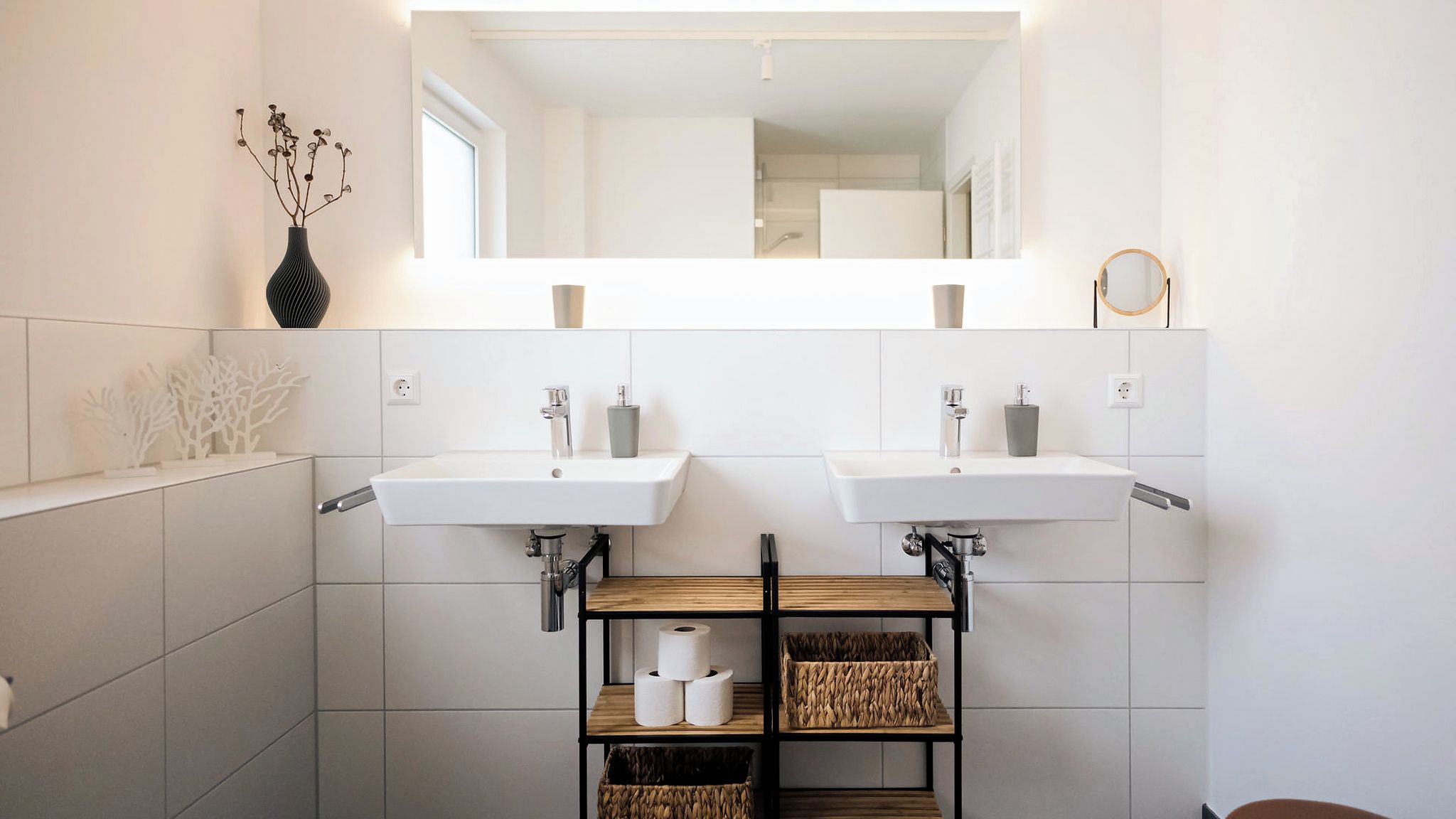 Un bagno moderno con due lavabi, uno specchio e uno scaffale con articoli da toilette.