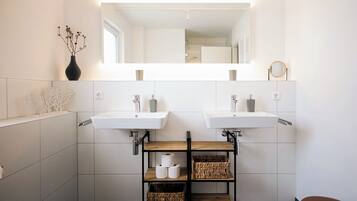 Un bagno moderno con due lavabi, uno specchio e uno scaffale con articoli da toilette.