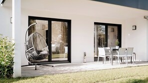 Un espace extérieur moderne aménagé avec des sièges, notamment un fauteuil suspendu, une table et des chaises.