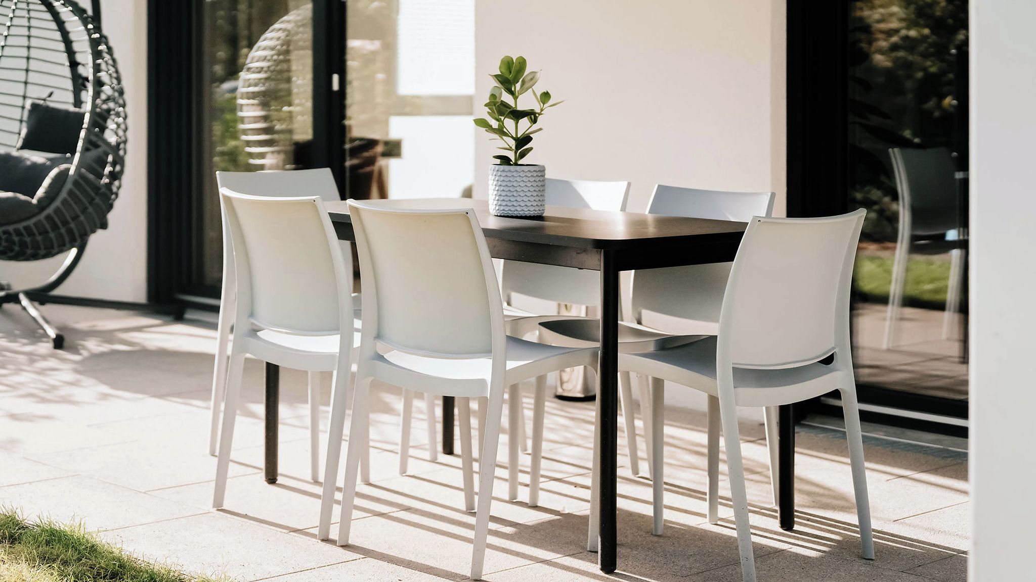 Un área de comedor al aire libre con una mesa, sillas, un sillón colgante y una planta en maceta.