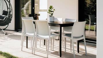 Un área de comedor al aire libre con una mesa, sillas, un sillón colgante y una planta en maceta.