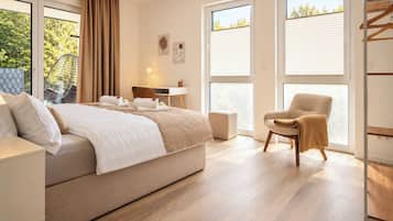 A hotel room with a bed, a chair, a desk, and large windows.