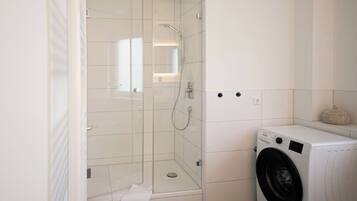 A bathroom with a glass-enclosed shower, a washing machine, and a small shelf with a decorative item.