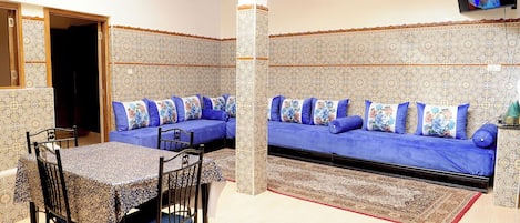 A dining area with a table and chairs, a sofa with blue cushions, and a patterned wall.