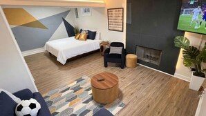 A modern living room with a bed, a TV, a fireplace, and a coffee table. - Large 4BR Home, Garage – Short & Long Stay (Pleasant Valley)