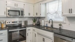 A modern kitchen with white cabinets, stainless steel appliances, a built-in oven, and a window with blinds. - Large 4BR Home, Garage – Short & Long Stay (Pleasant Valley)