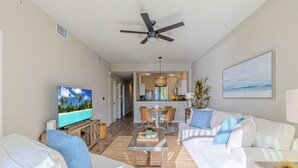 A modern living room with a flat-screen TV, white sofas, and a ceiling fan. - Rare NEW 2/2 Condo in Naples with Lake & Golf View! Home Away from Home (Naples)