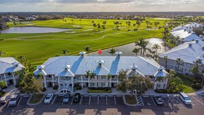 A large hotel with a central courtyard, multiple parking spaces, and a golf course in the background. - Rare NEW 2/2 Condo in Naples with Lake & Golf View! Home Away from Home (Naples)