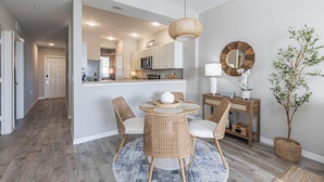 A modern kitchen with white cabinets, a microwave, and a dining area with wicker chairs and a round table. - Rare NEW 2/2 Condo in Naples with Lake & Golf View! Home Away from Home (Naples)