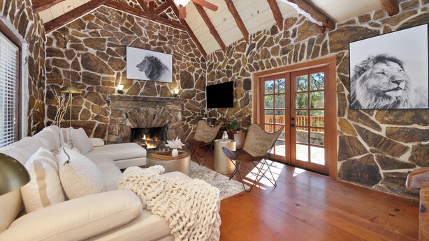 A cozy living room with a stone fireplace, comfortable seating, and a large window.