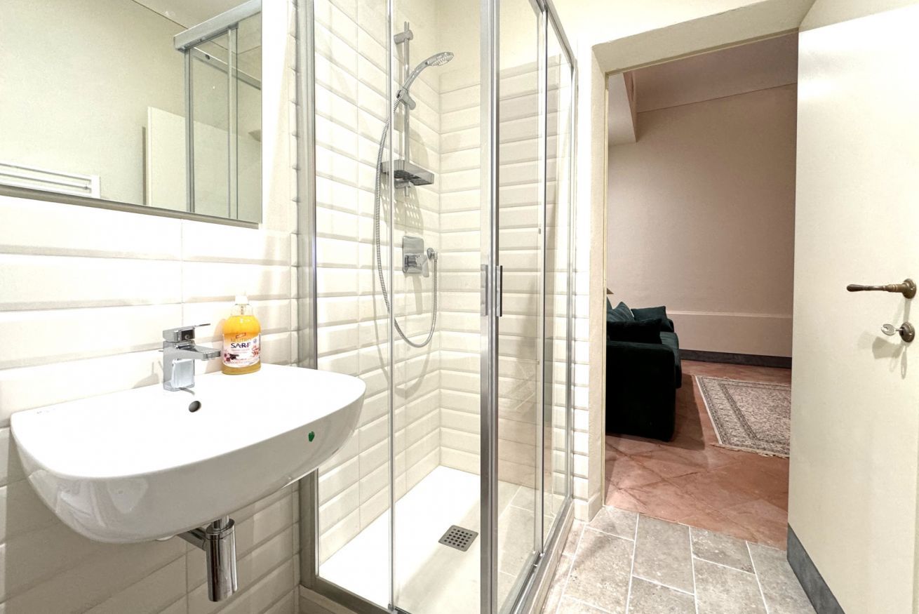 Een badkamer met een wit wastafelmeubel, een douchecabine van glas en een spiegel.