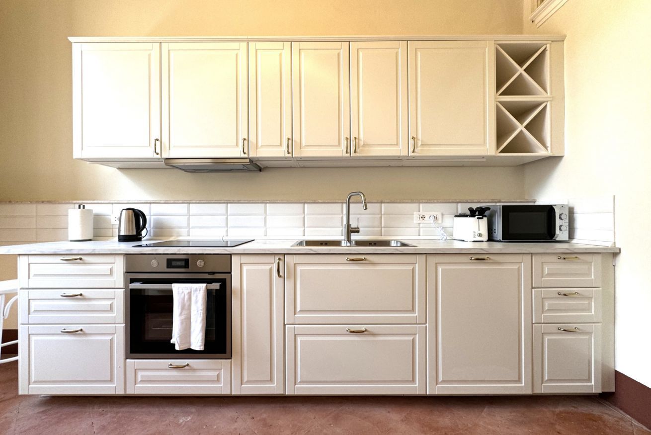 Una cocina con gabinetes blancos, microondas, hervidor y tostadora.