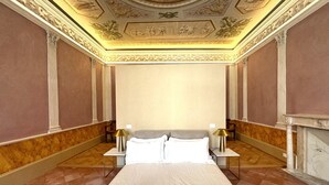 Ein Hotelzimmer mit einem großen Bett, zwei Nachttischen mit Lampen, Marmorboden und einer dekorativen Decke.